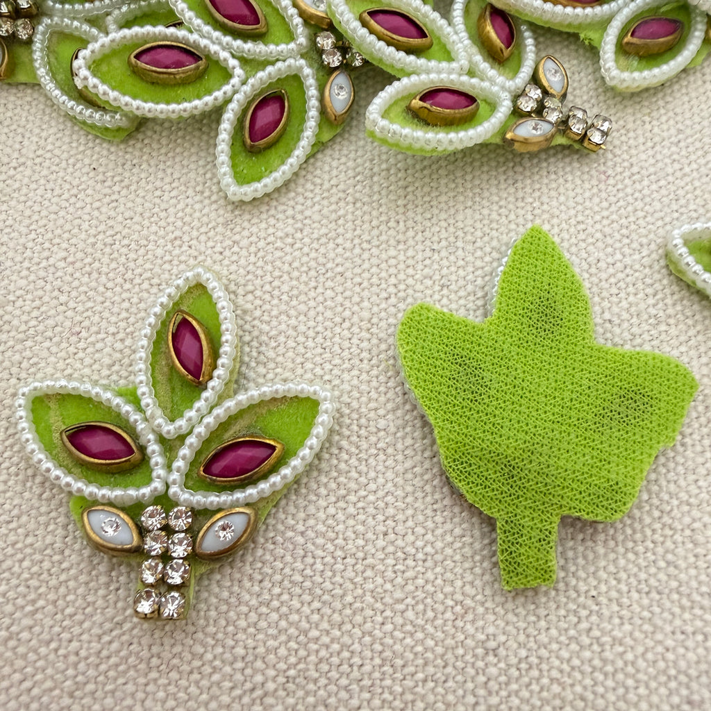 Decorative green leaf-shaped brooches with gemstones on a textured beige surface