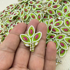Decorative green and pink brooch held between fingers with a detailed embroidered background.
