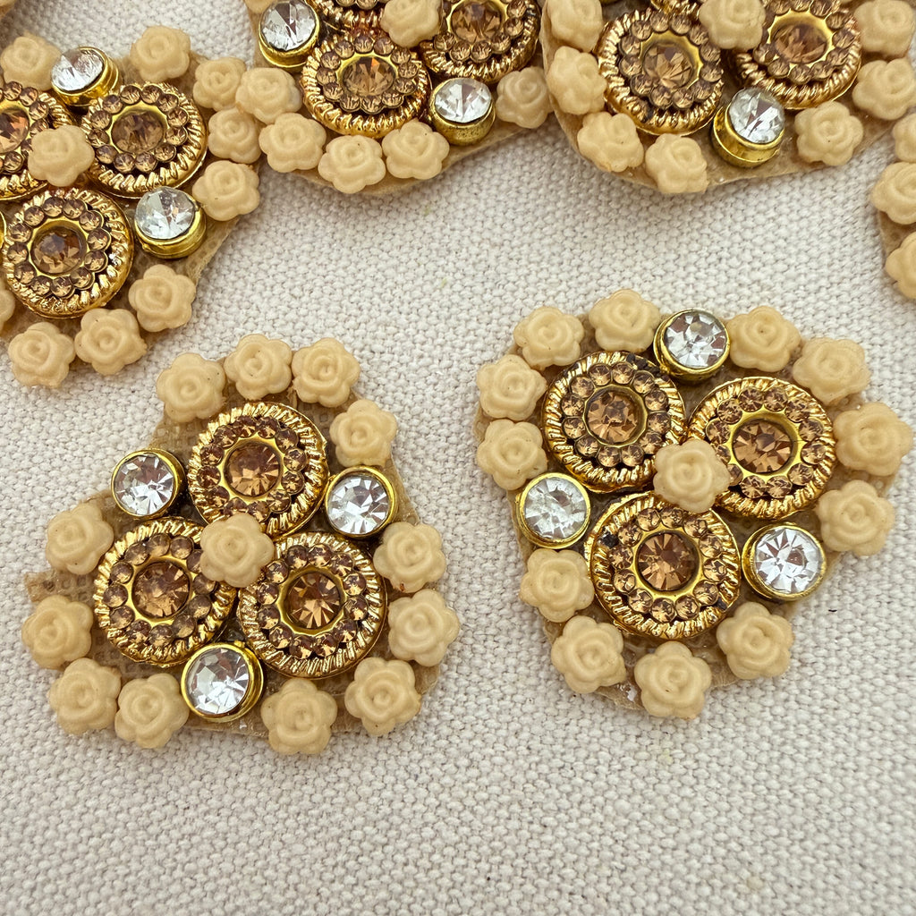 Pair of gold and beige earrings with floral designs on a textured surface