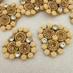 Pair of gold and beige earrings with floral designs on a textured surface
