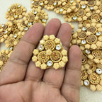 Decorative gold and beige embellishment held between fingers with a background of similar embellishments.