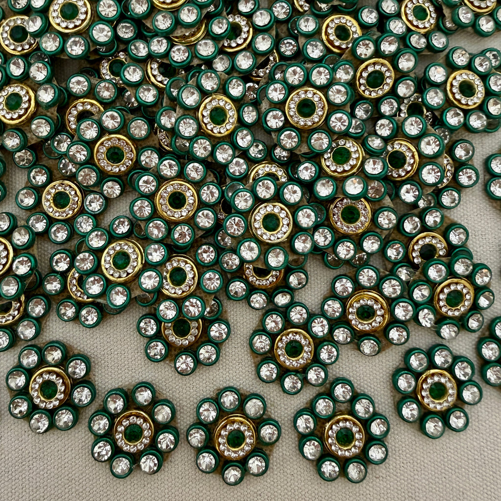 Close-up of decorative embellishments with green, gold, and clear stones on a gray background