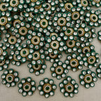 Close-up of decorative embellishments with green, gold, and clear stones on a gray background