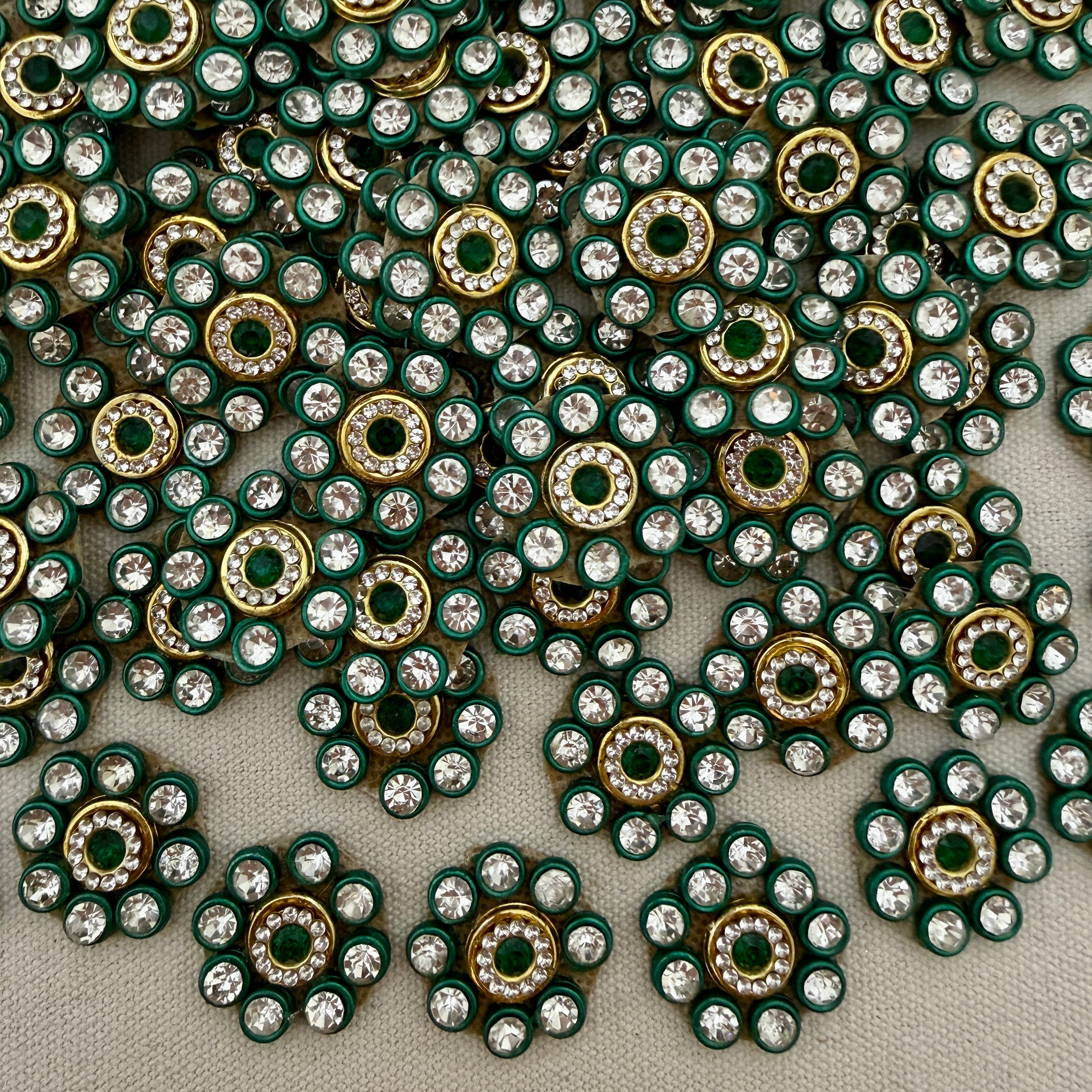 Close-up of decorative embellishments with green, gold, and clear stones on a gray background