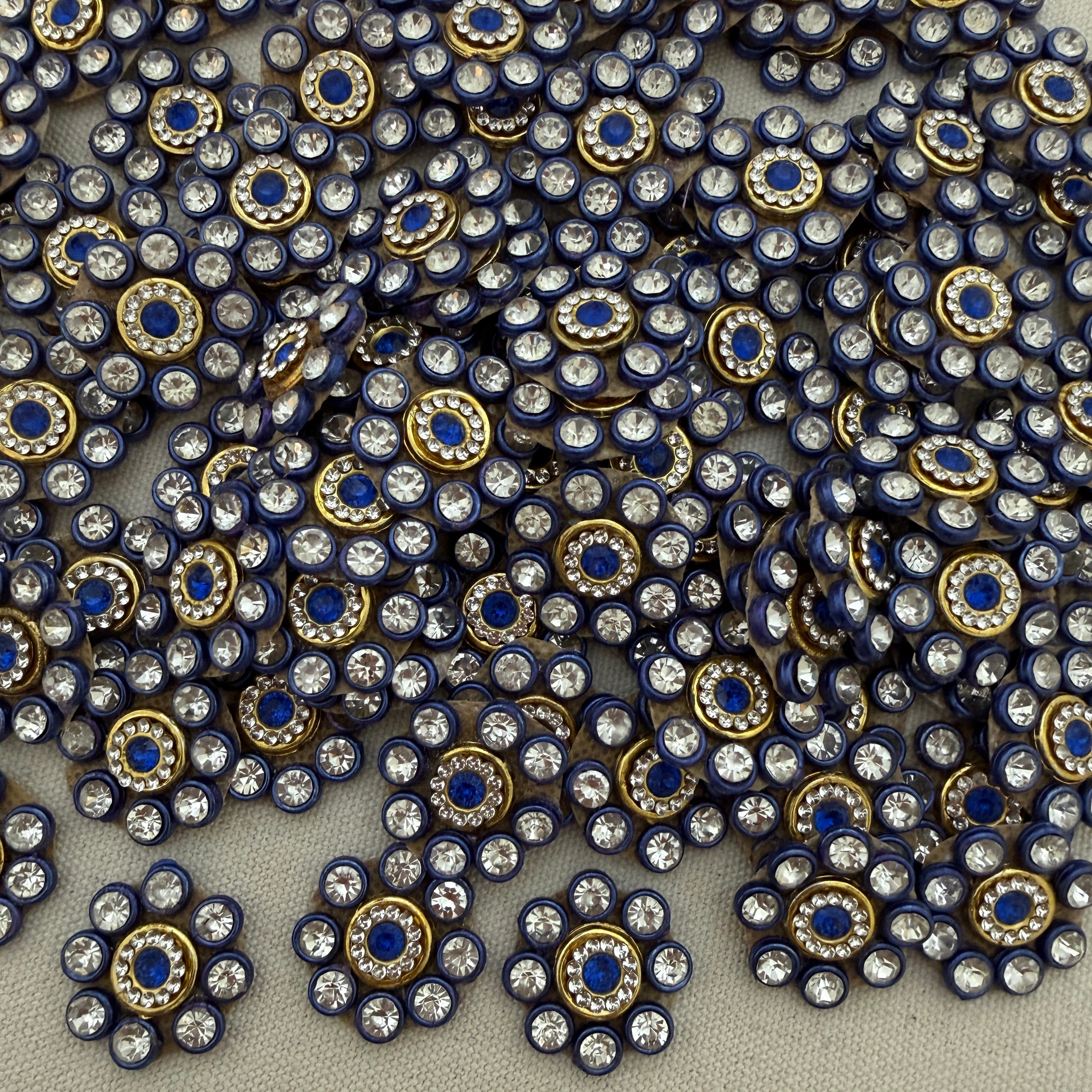 Close-up of decorative embellishments with blue centers and gold and silver accents on a neutral background.