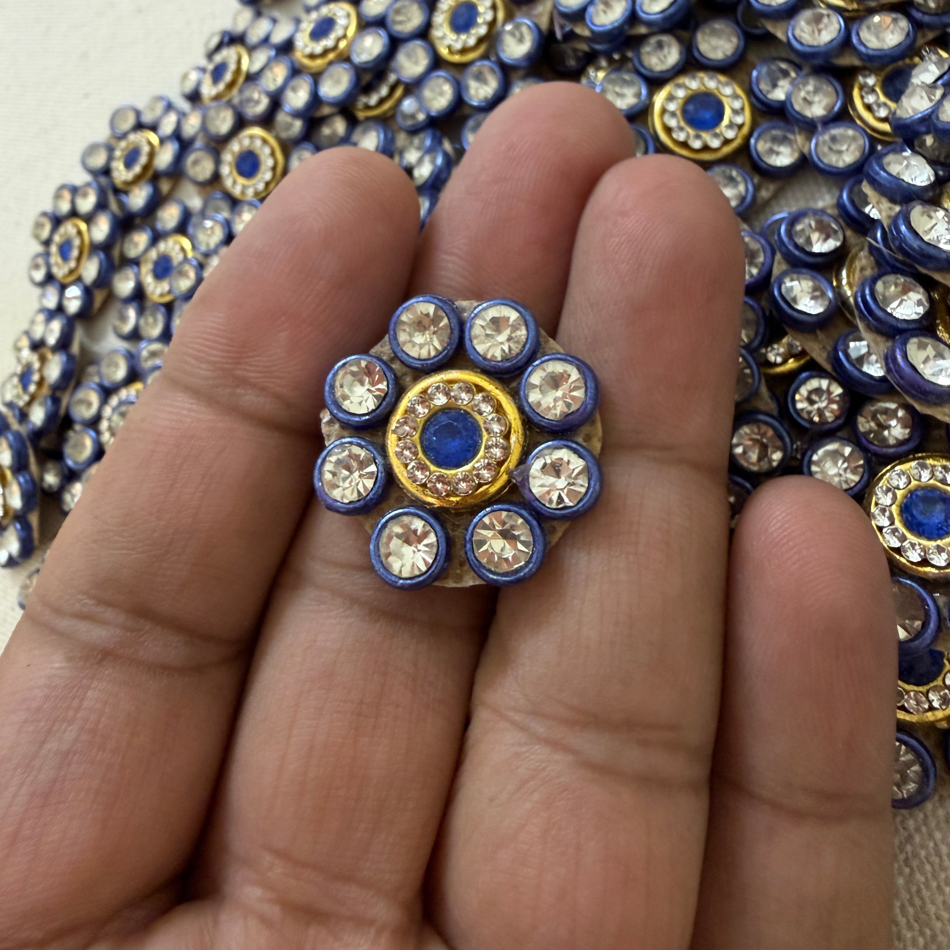 Close-up of a hand holding a decorative button with blue and gold accents.