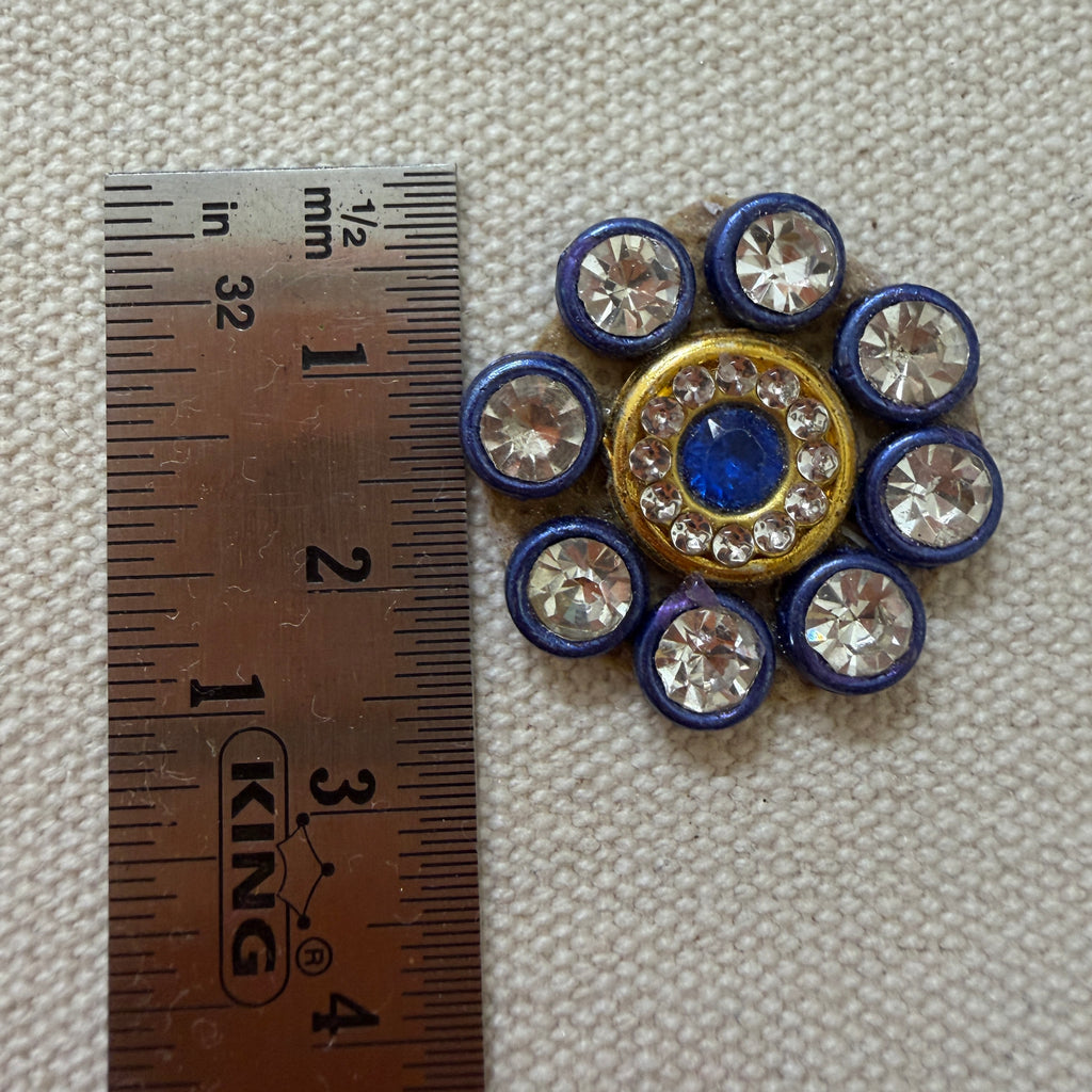 Decorative button with blue and gold center and surrounding crystals, next to a ruler for scale.