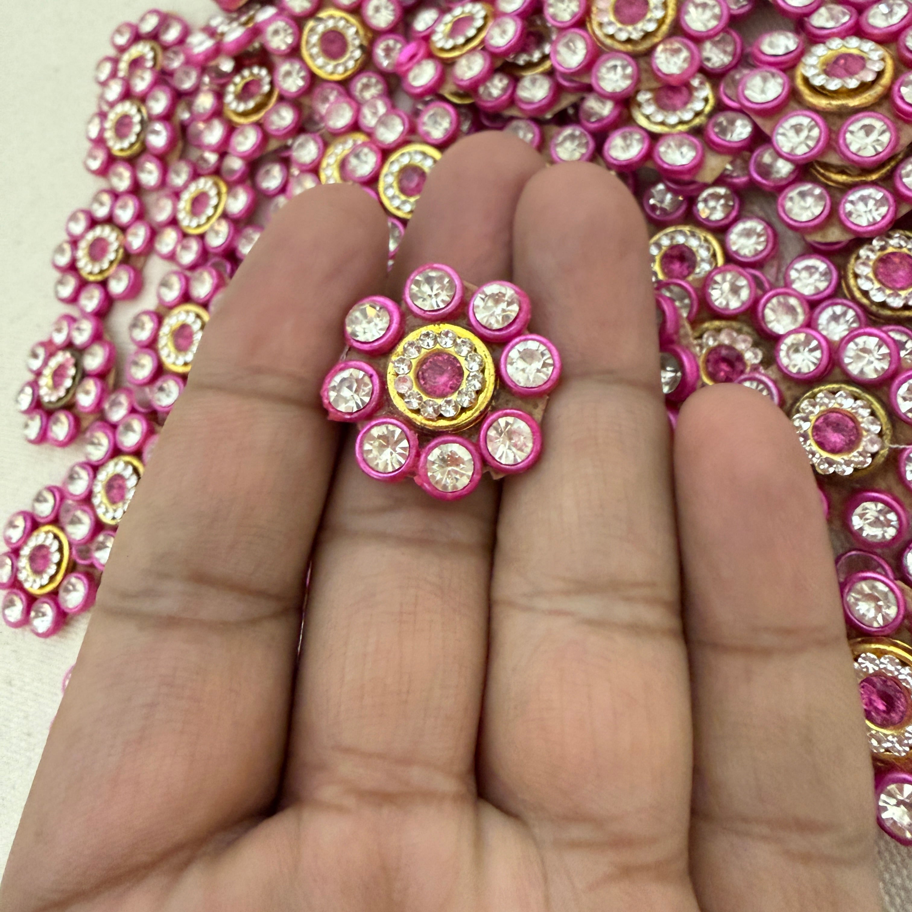 Decorative pink and gold embellishment on a hand with a pink rhinestone background
