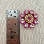 Decorative button with pink and gold accents next to a ruler on a textured surface