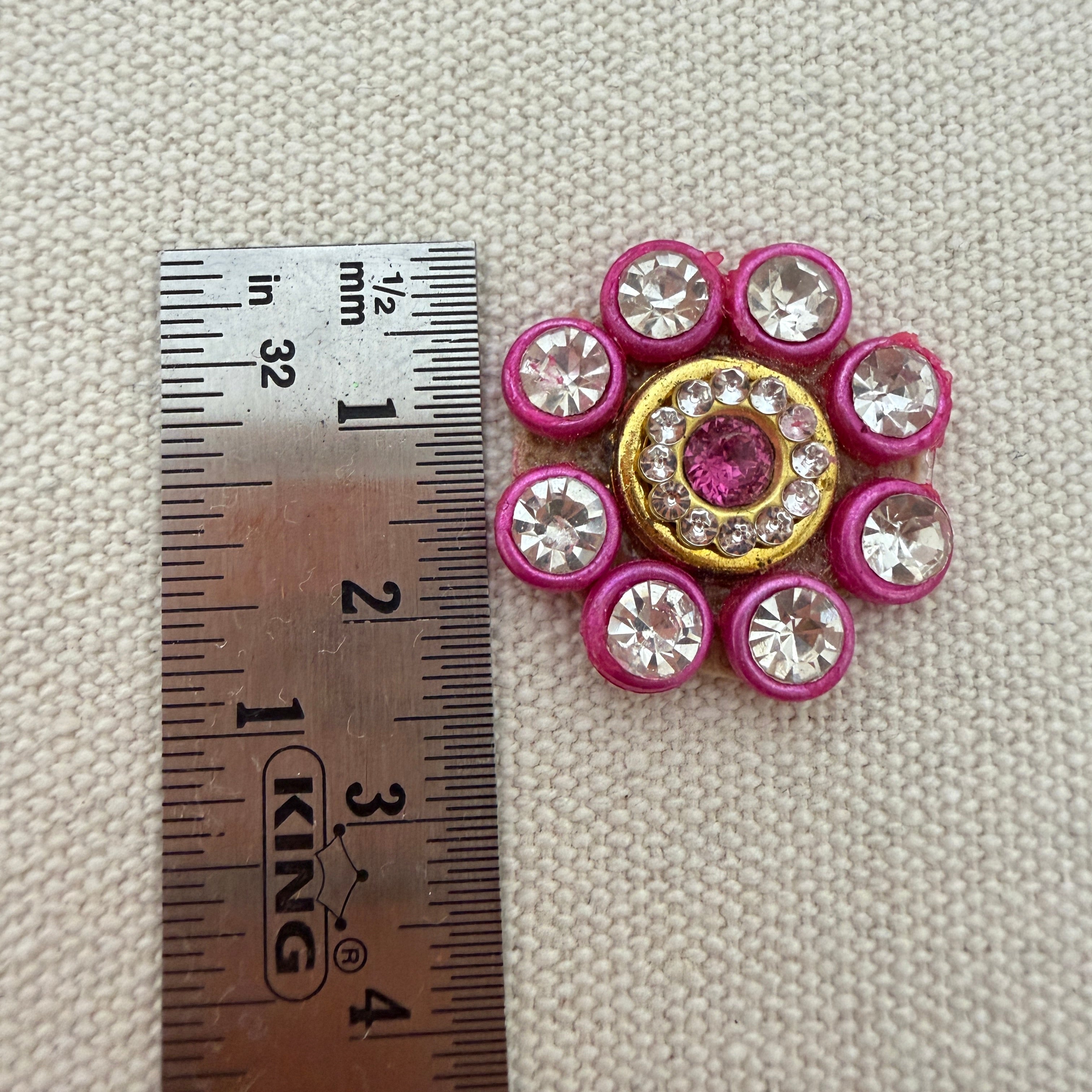Decorative button with pink and gold accents next to a ruler on a textured surface
