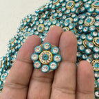 Close-up of a decorative button with blue and gold accents held between fingers.