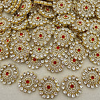 Close-up of decorative circular embellishments with gold, red, and clear stones on a beige background