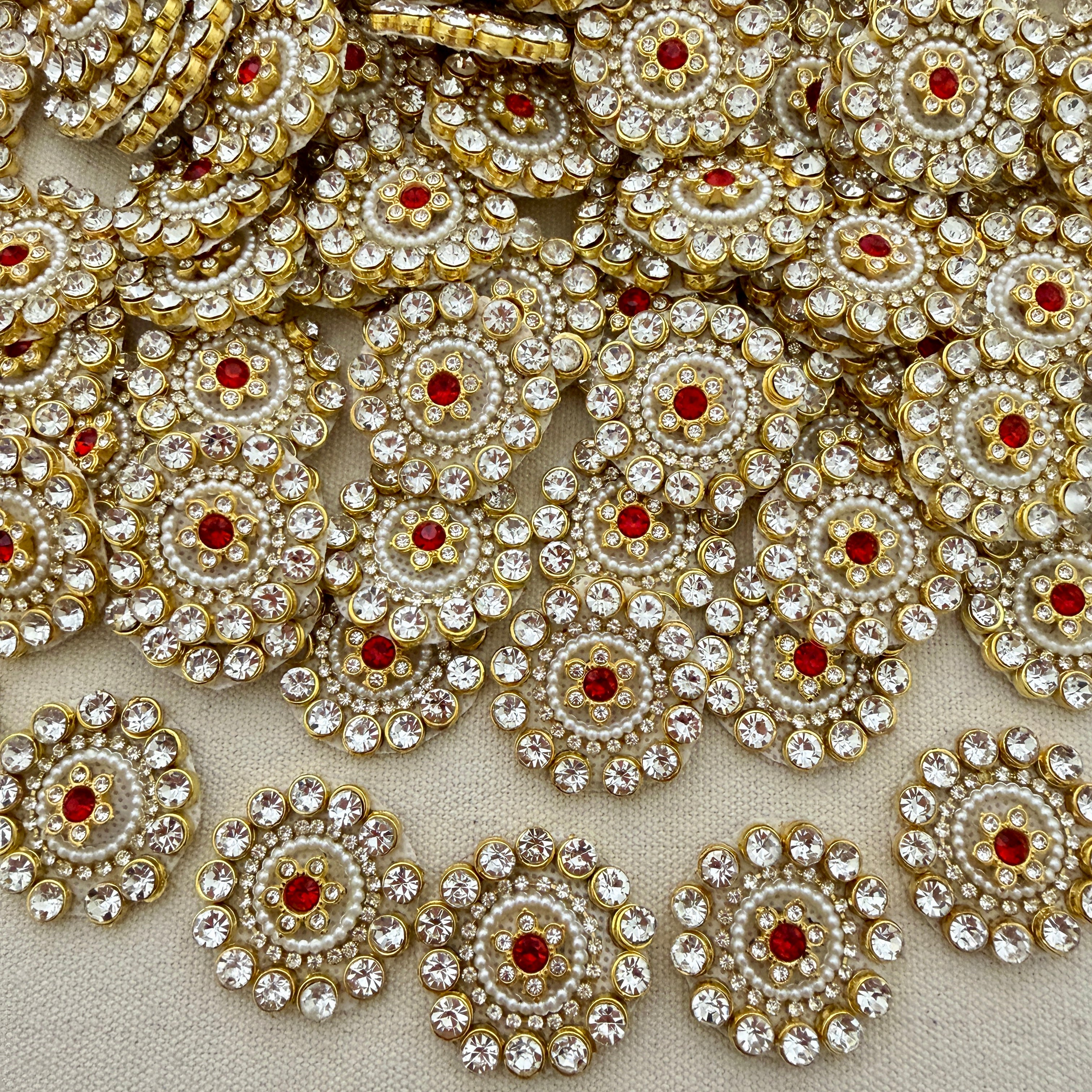 Close-up of decorative circular embellishments with gold, red, and clear stones on a beige background