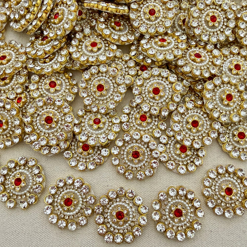Close-up of decorative circular embellishments with gold, red, and clear stones on a beige background