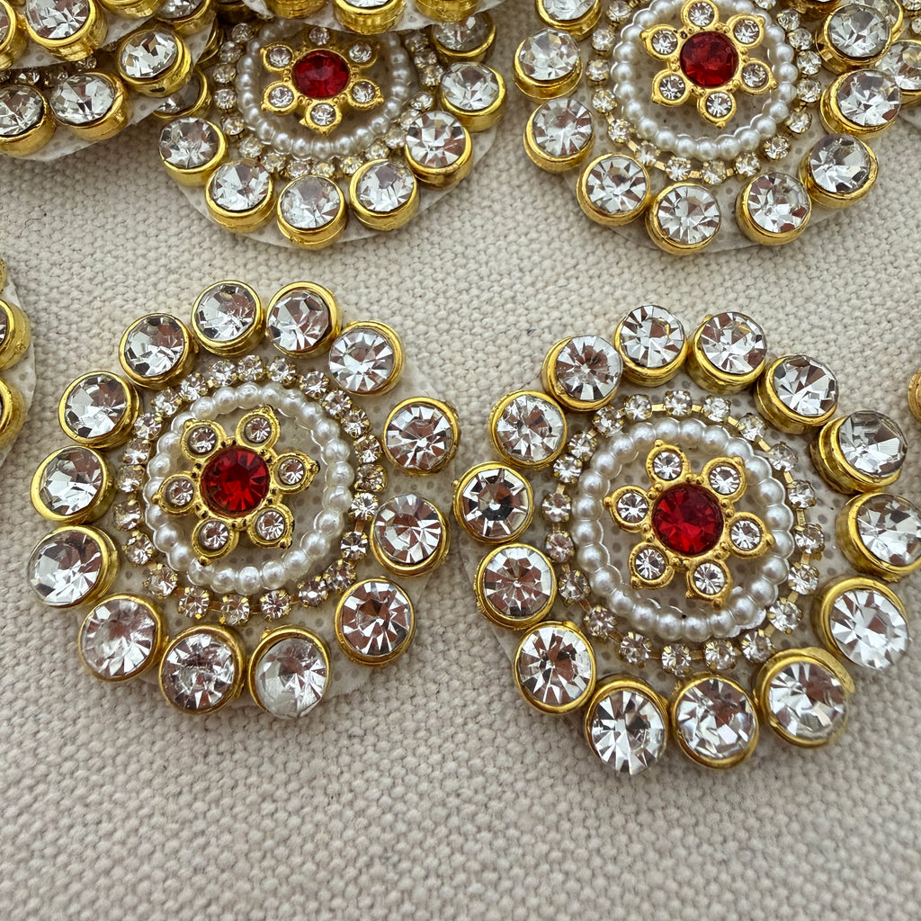 Decorative brooches with gold, red, and pearl details on a textured surface