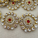 Decorative brooches with gold, red, and pearl details on a textured surface