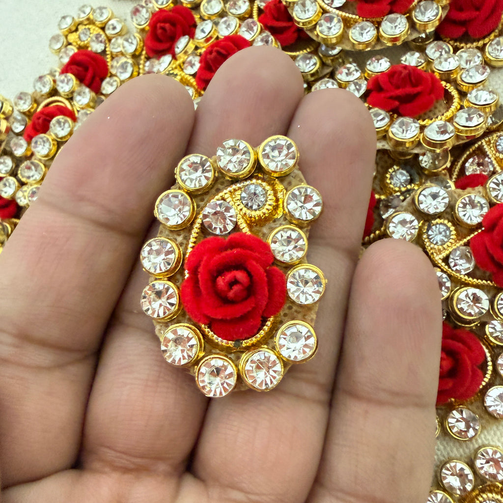 Decorative brooch with red rose and crystals held between fingers against a decorative background.