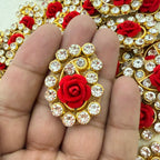 Decorative brooch with red rose and crystals held between fingers against a decorative background.