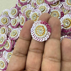 Decorative circular embellishments with pink, white, and gold colors on a hand.