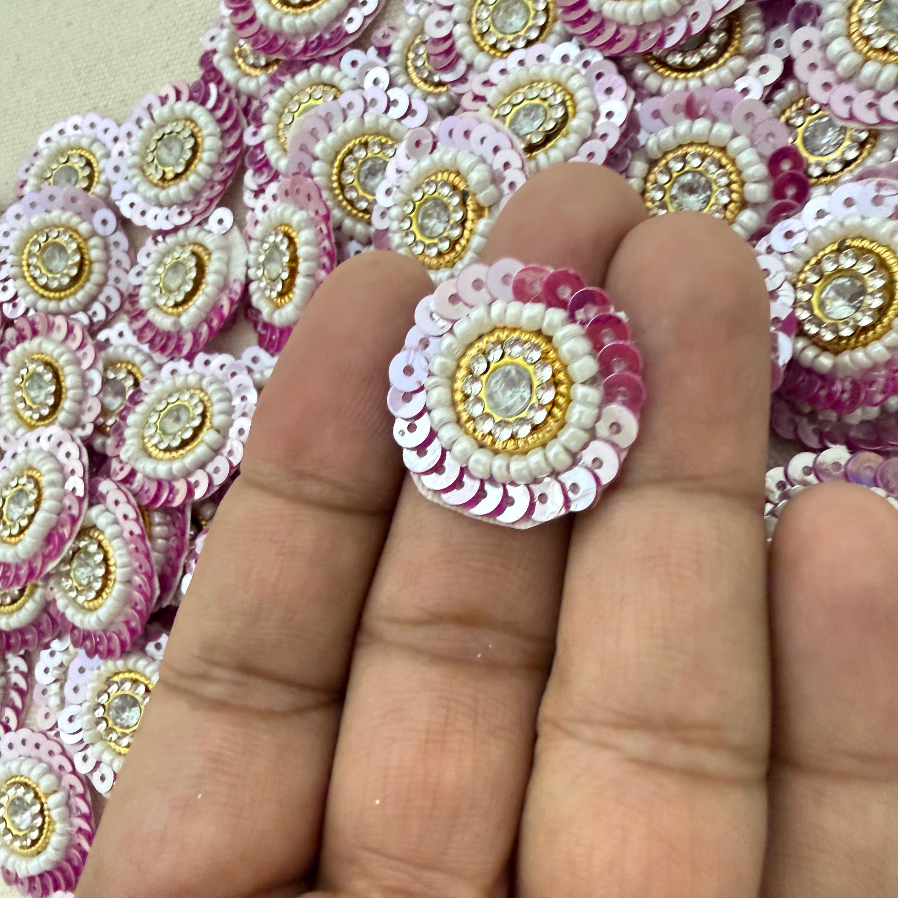 Decorative circular embellishments with pink, white, and gold colors on a hand.