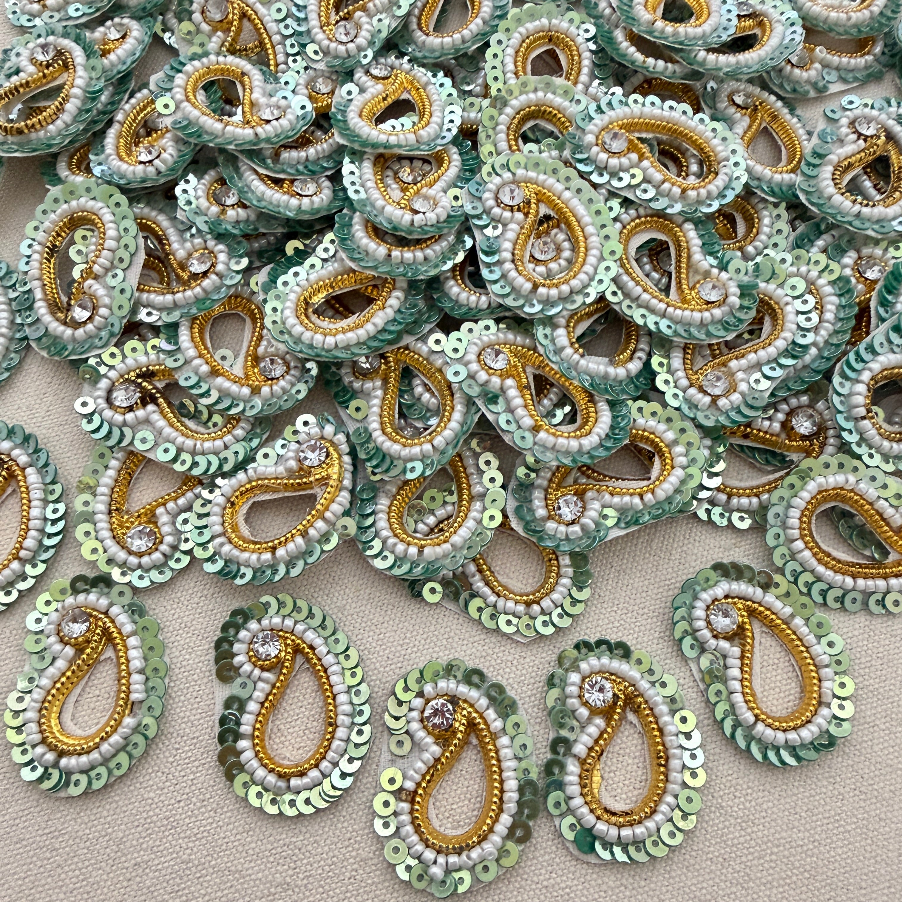 Collection of green and gold beaded paisley designs on a beige background