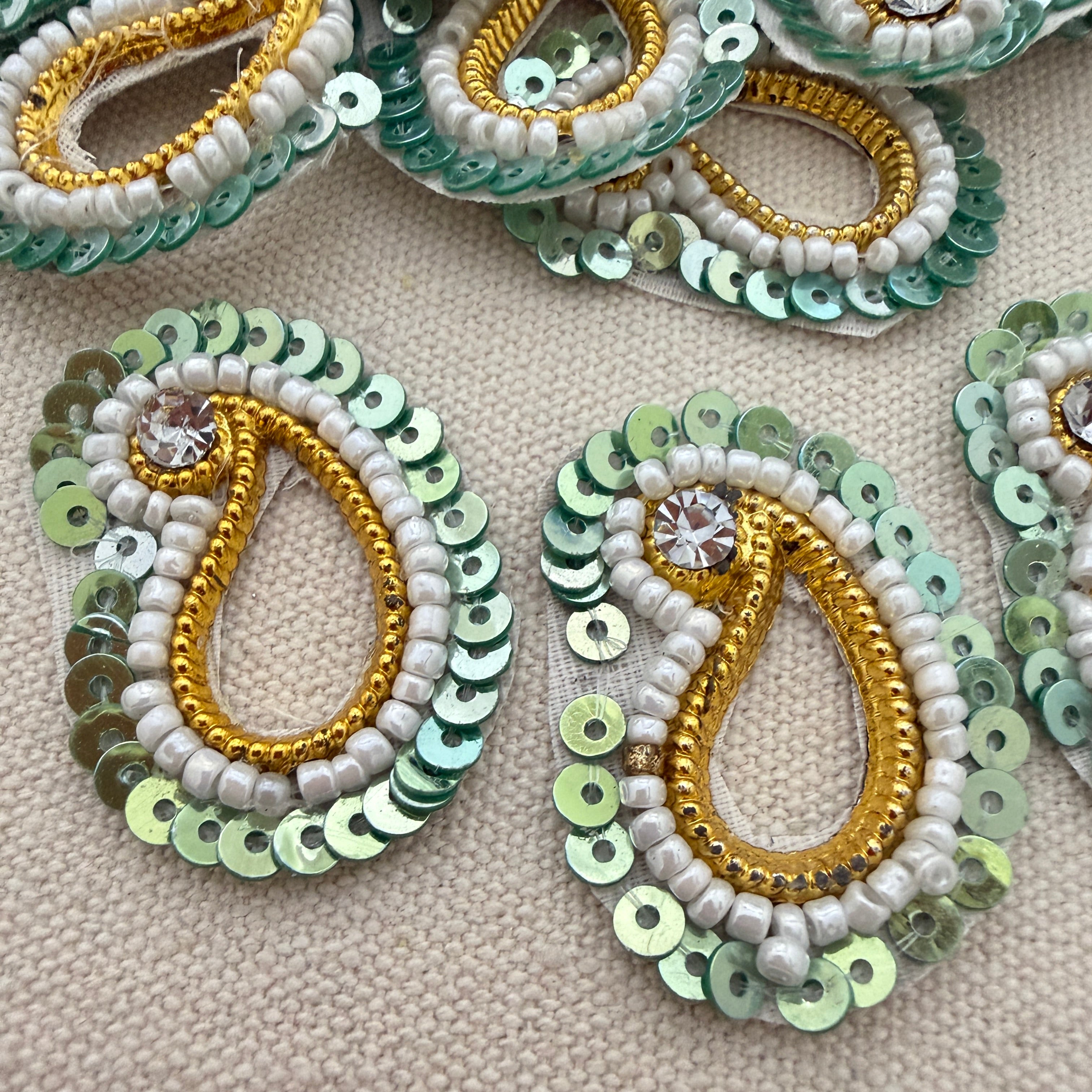 Decorative earrings with sequins and beads on a beige fabric background