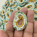 Decorative beaded earring held between fingers with a background of similar earrings.