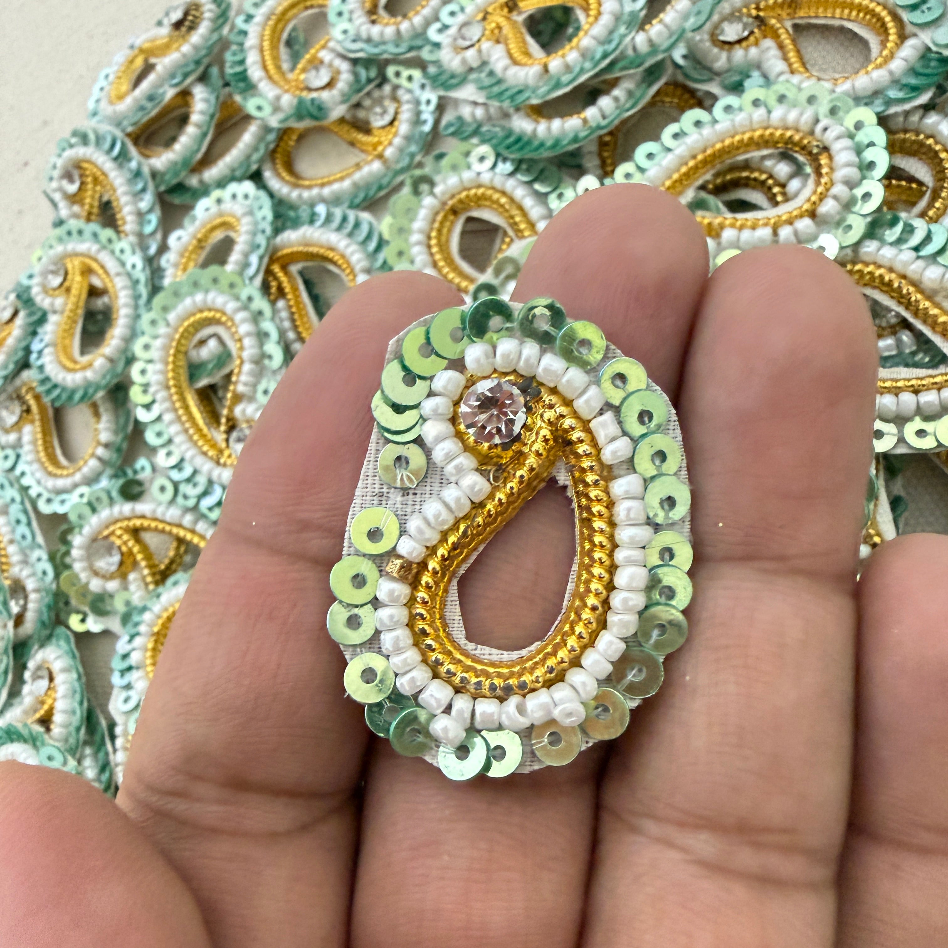 Decorative beaded earring held between fingers with a background of similar earrings.