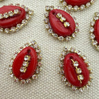 Red oval stones with gold and clear gemstone accents on a textured beige background