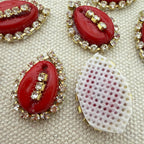 Red oval stones with gold and clear gemstone accents on a textured beige background