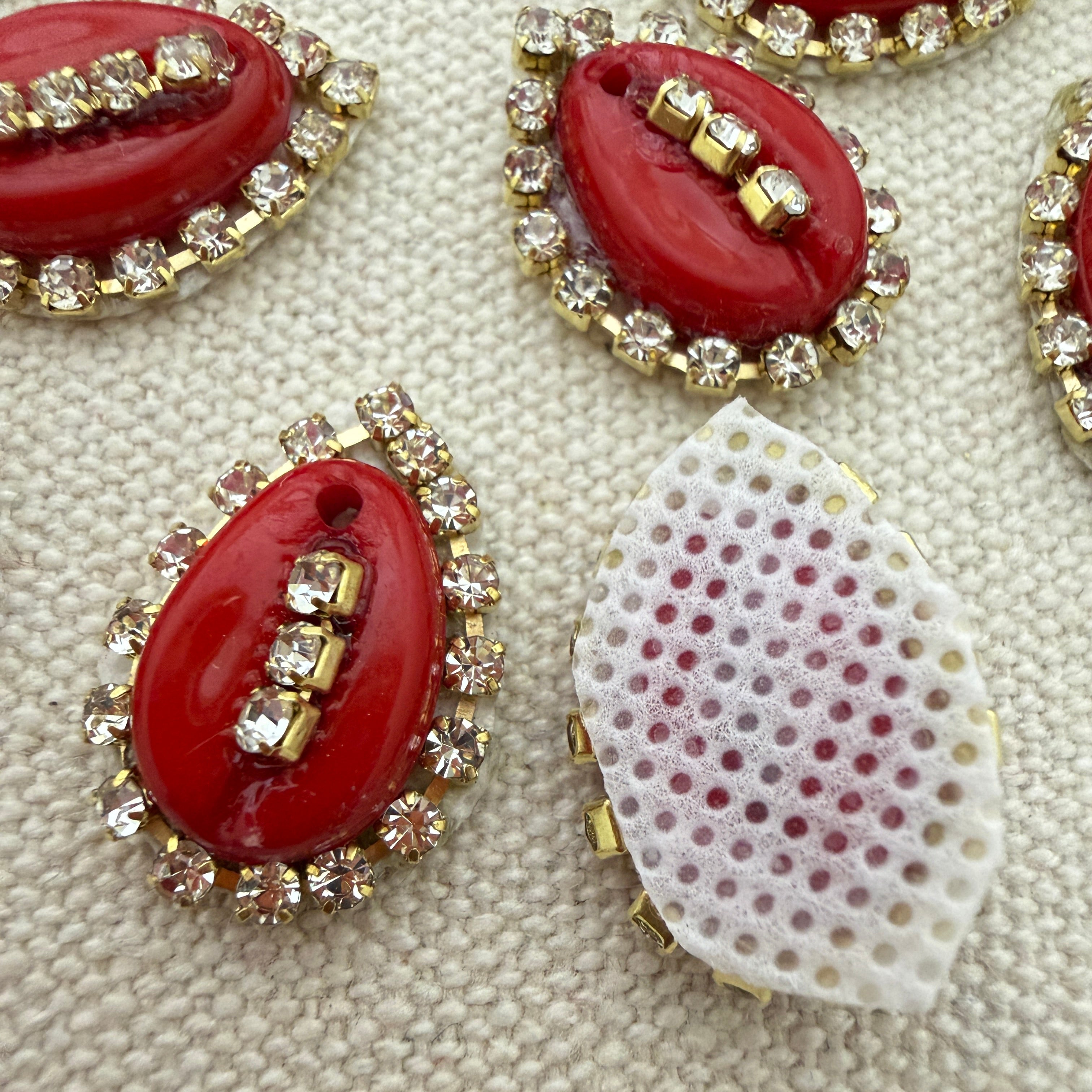Red oval stones with gold and clear gemstone accents on a textured beige background