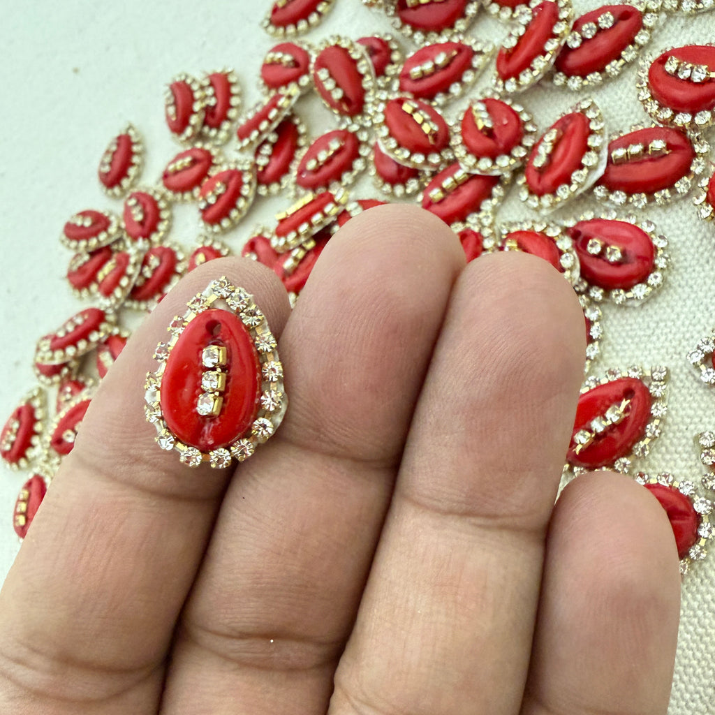 Red and gold decorative item on a finger with a pattern of similar items in the background