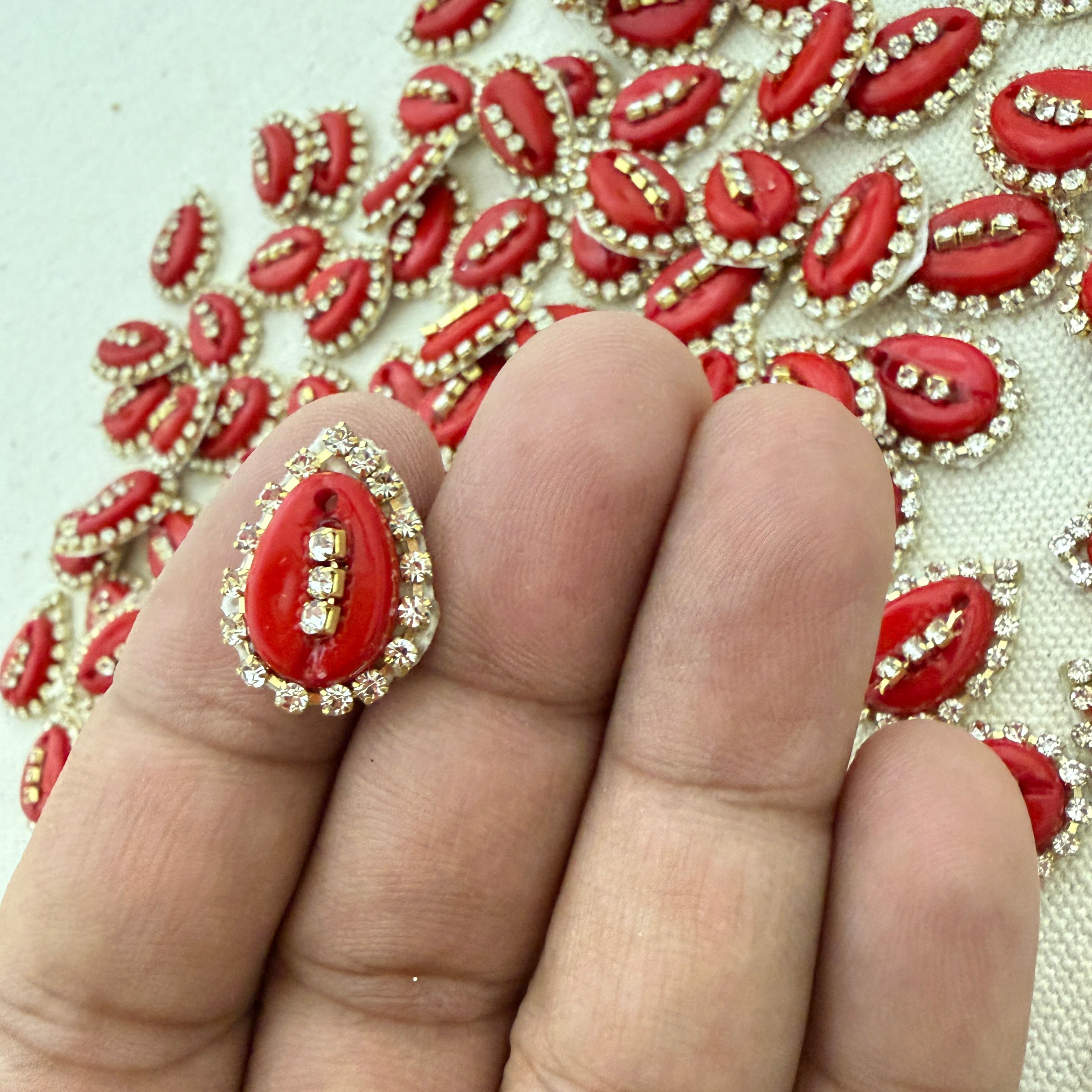 Red and gold decorative item on a finger with a pattern of similar items in the background