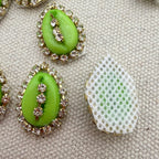 Green teardrop-shaped earrings with rhinestone details on a textured surface.
