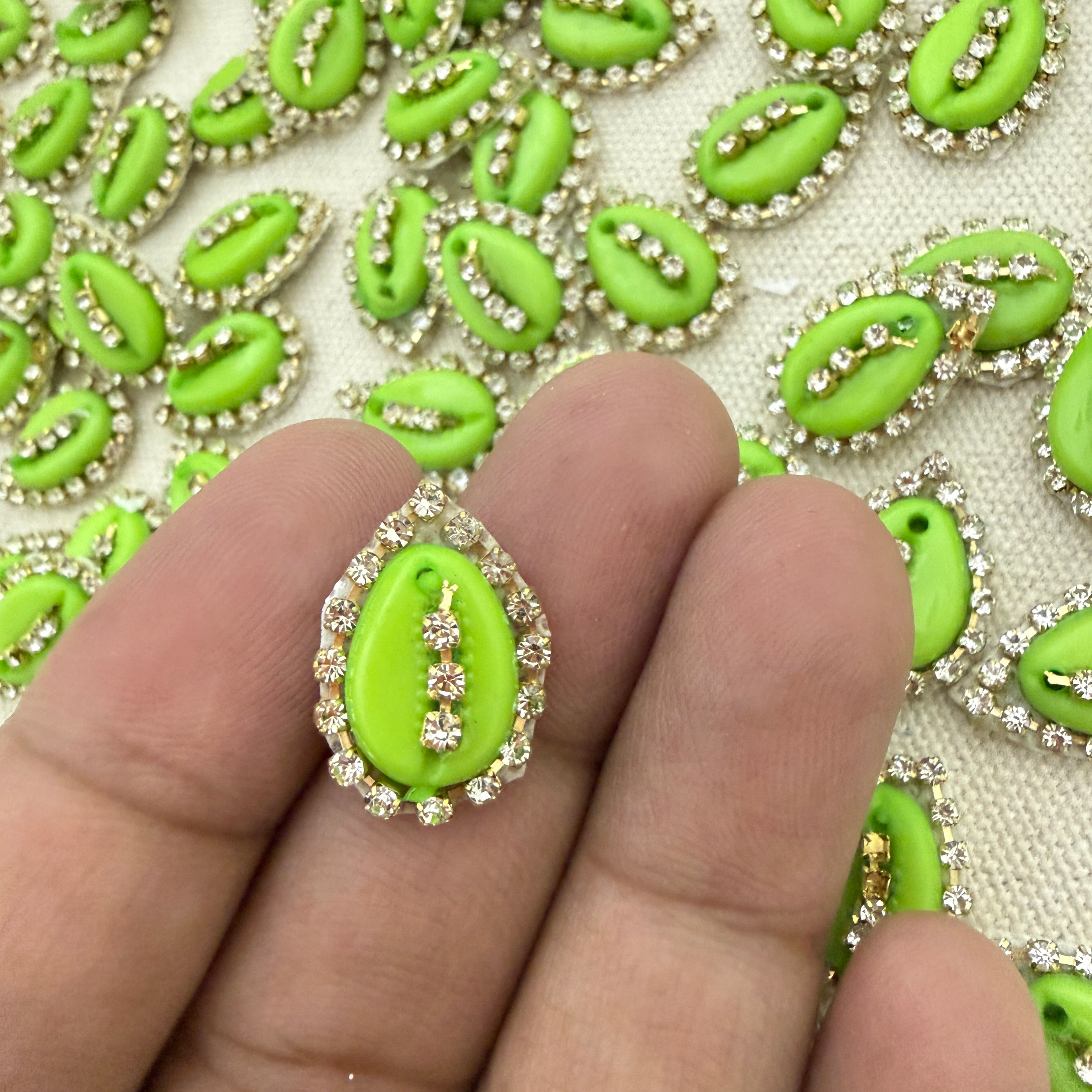 Close-up of a hand holding a green decorative item with rhinestones against a patterned background.