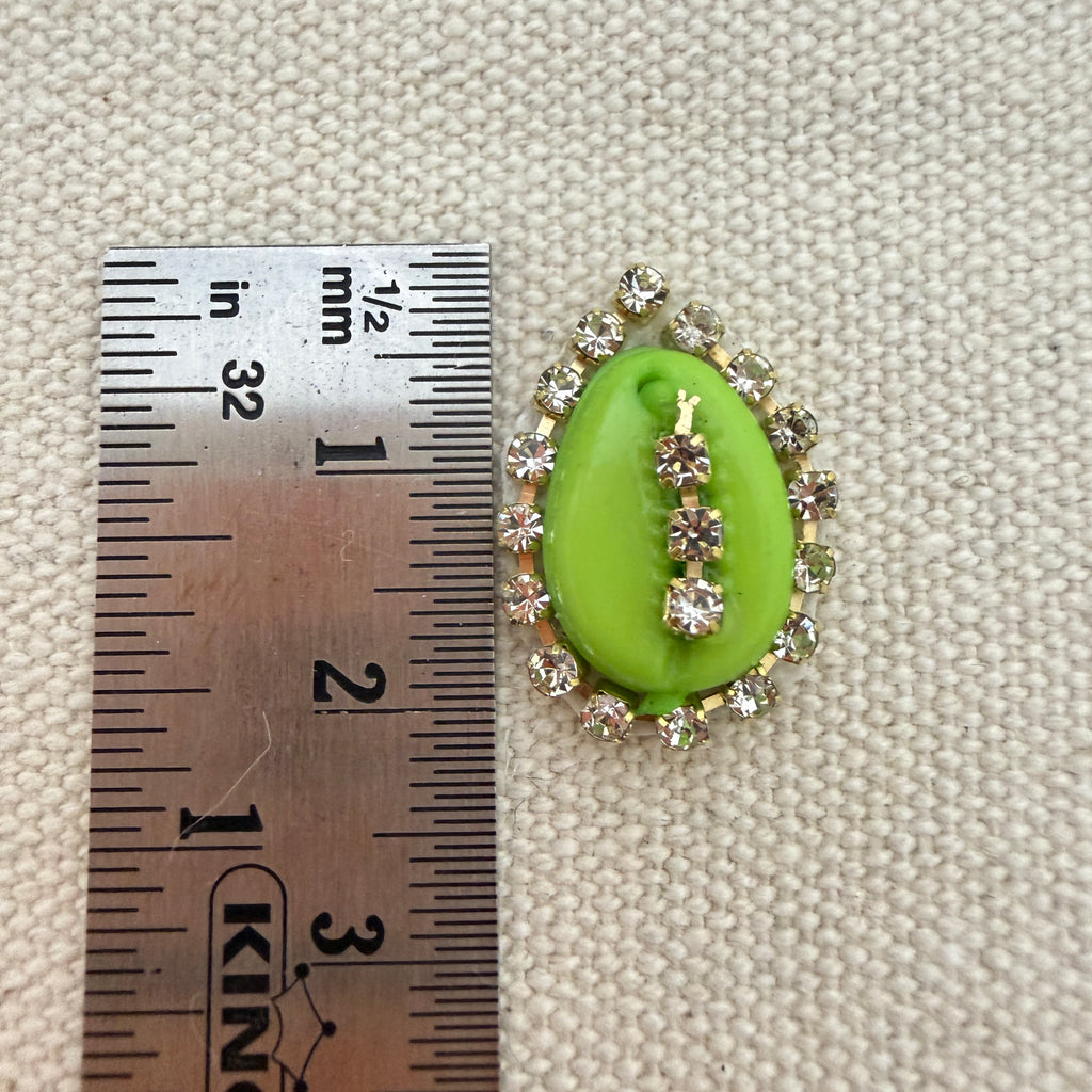 Green gemstone with rhinestones next to a ruler on a textured beige background
