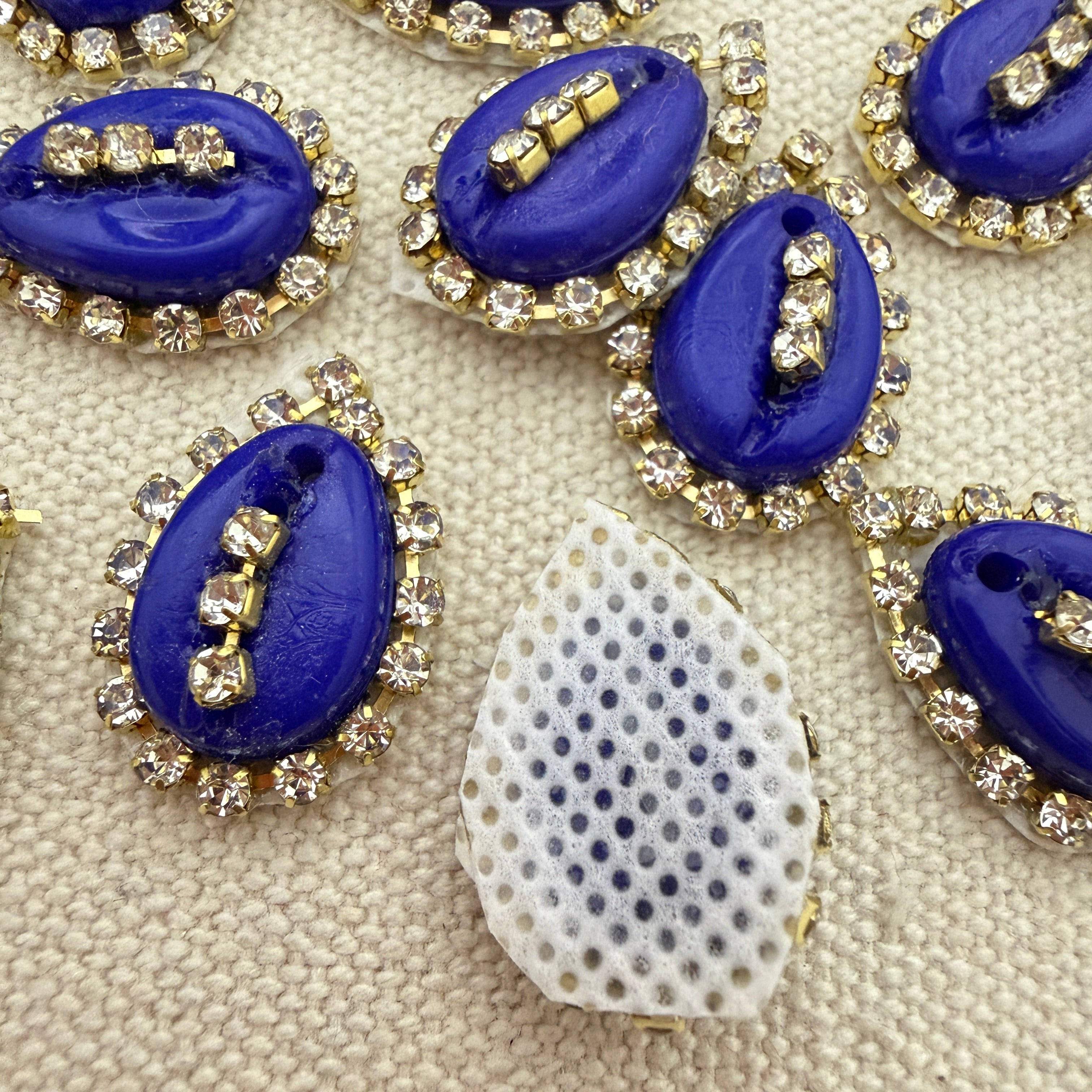 Blue teardrop-shaped embellishments with rhinestones on a textured beige surface