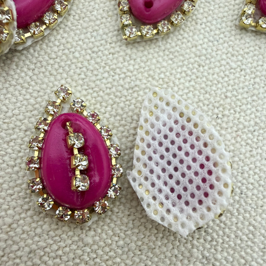 Pink gemstone with gold and crystal embellishments on a textured beige background