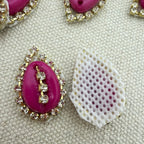 Pink gemstone with gold and crystal embellishments on a textured beige background