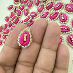 Pink lip-shaped embellishment with rhinestones on a hand, with a pattern of similar embellishments in the background.