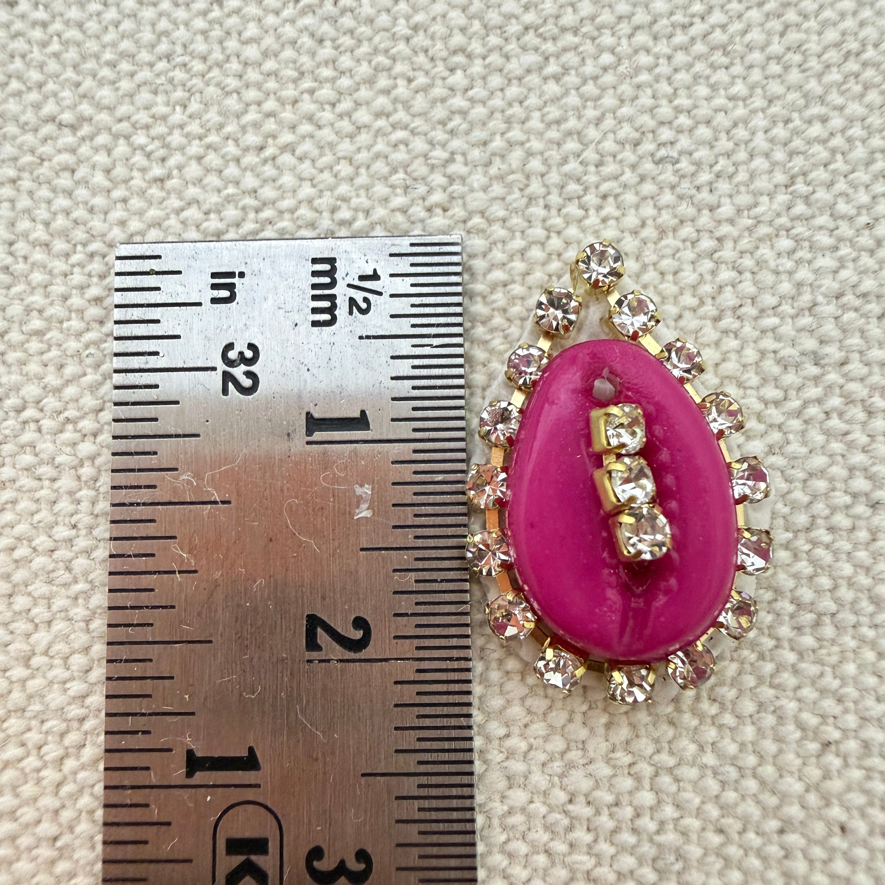 Pink brooch with gemstone measurements against a textured beige background