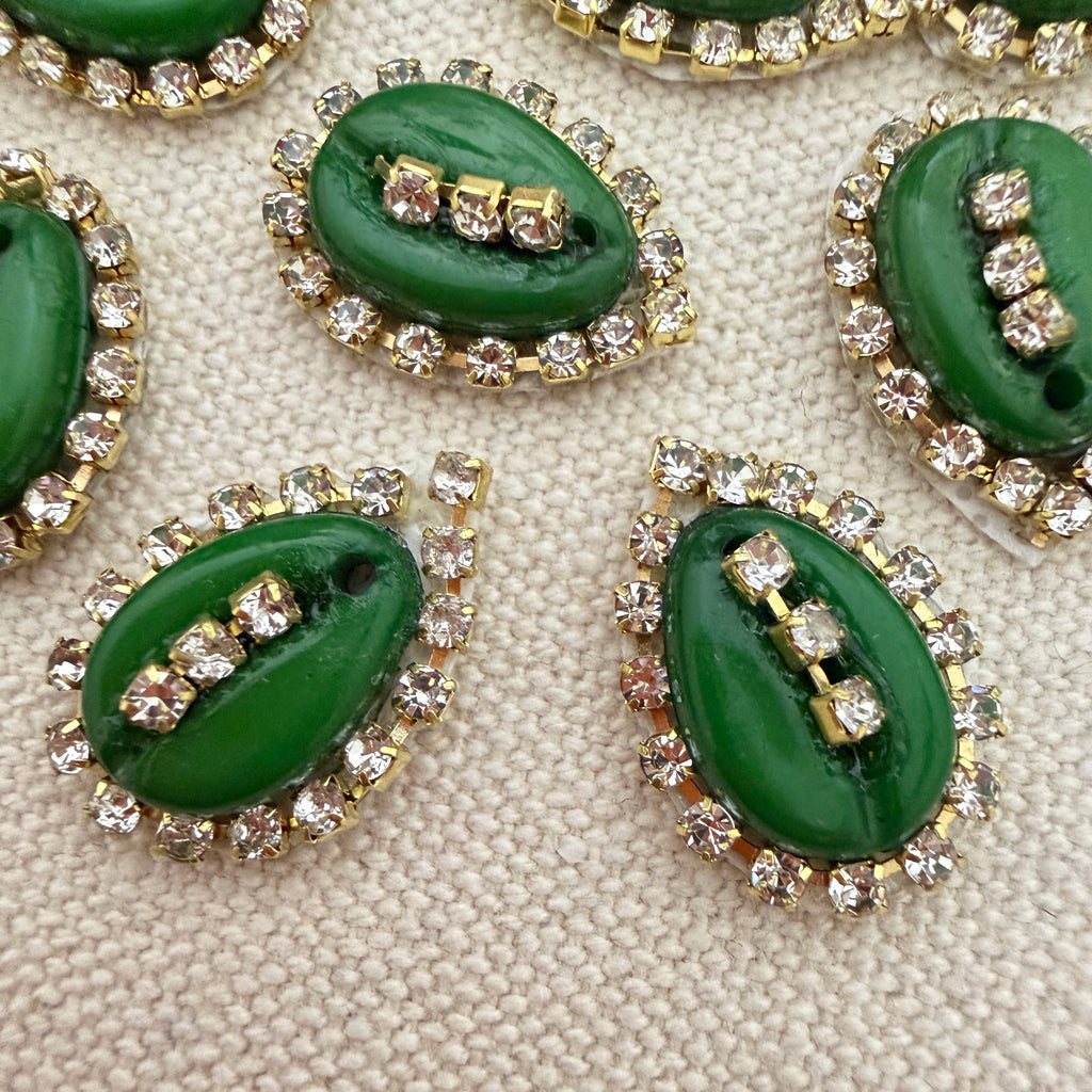 Green buttons with gold and clear gemstone embellishments on a textured beige surface
