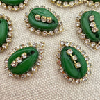 Green buttons with gold and clear gemstone embellishments on a textured beige surface
