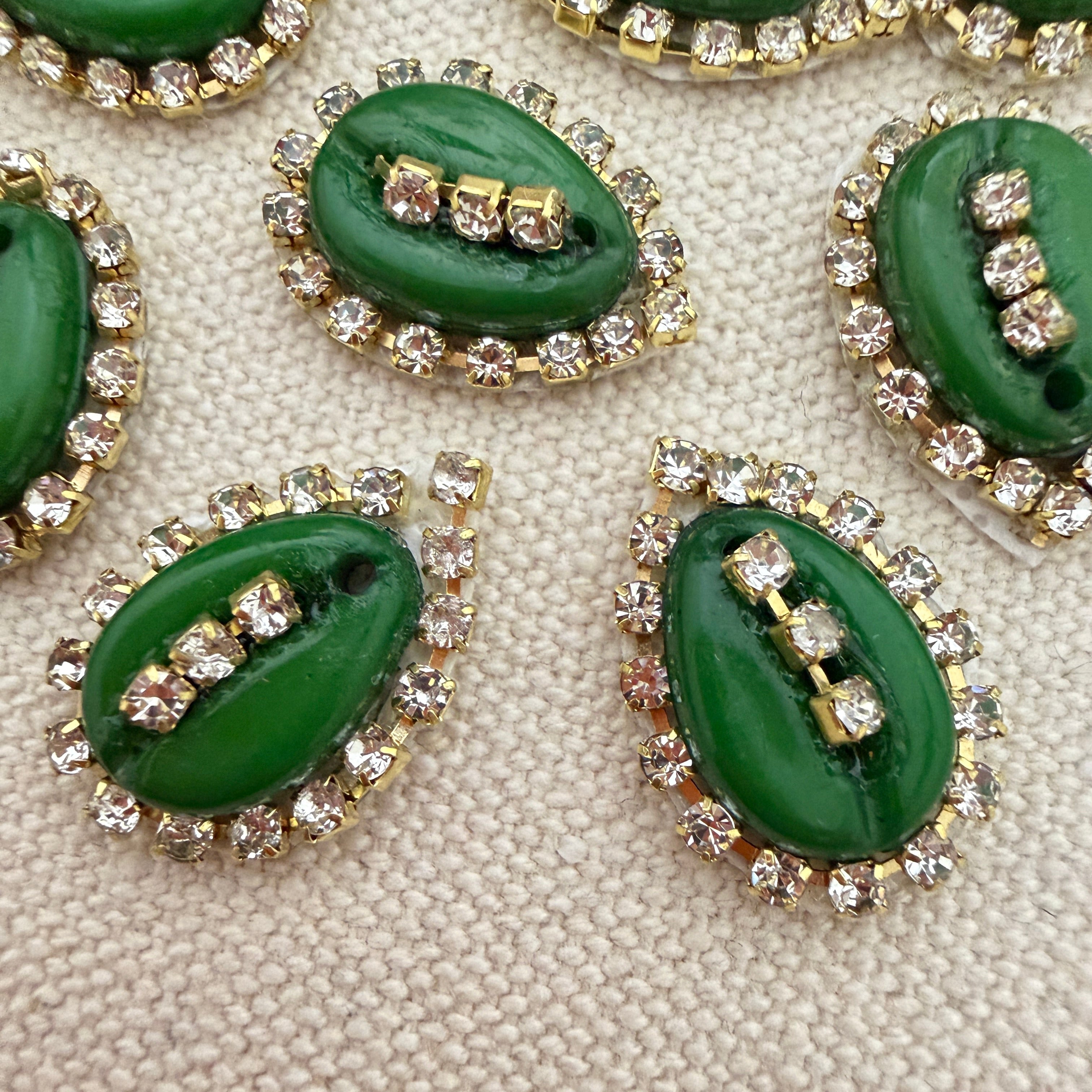 Green buttons with gold and clear gemstone embellishments on a textured beige surface