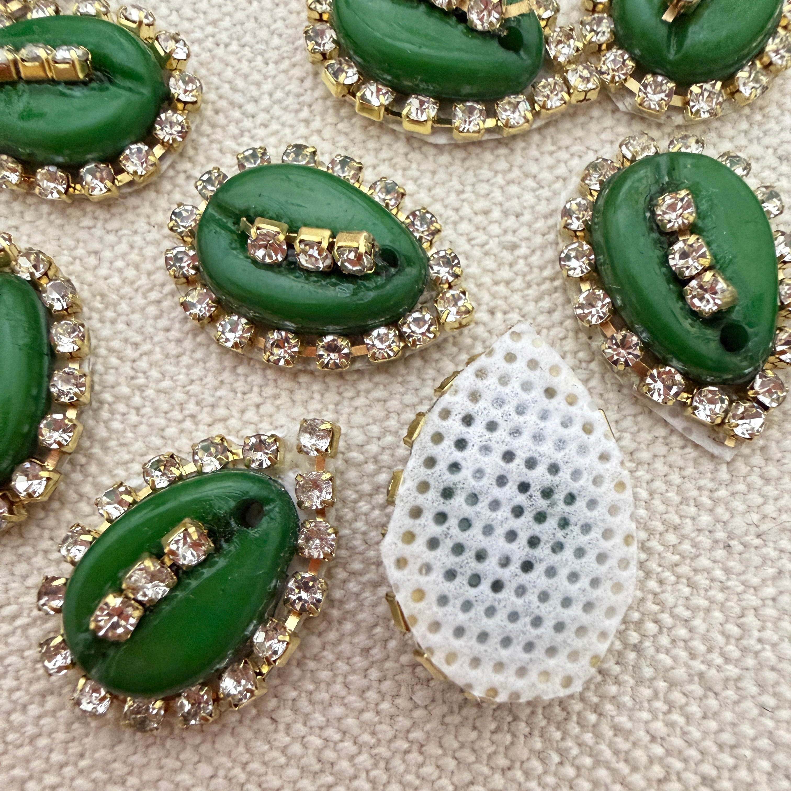 Green leaf-shaped buttons with rhinestone accents on a textured beige background