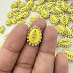 Yellow decorative element with rhinestones held between fingers against a background of similar elements.