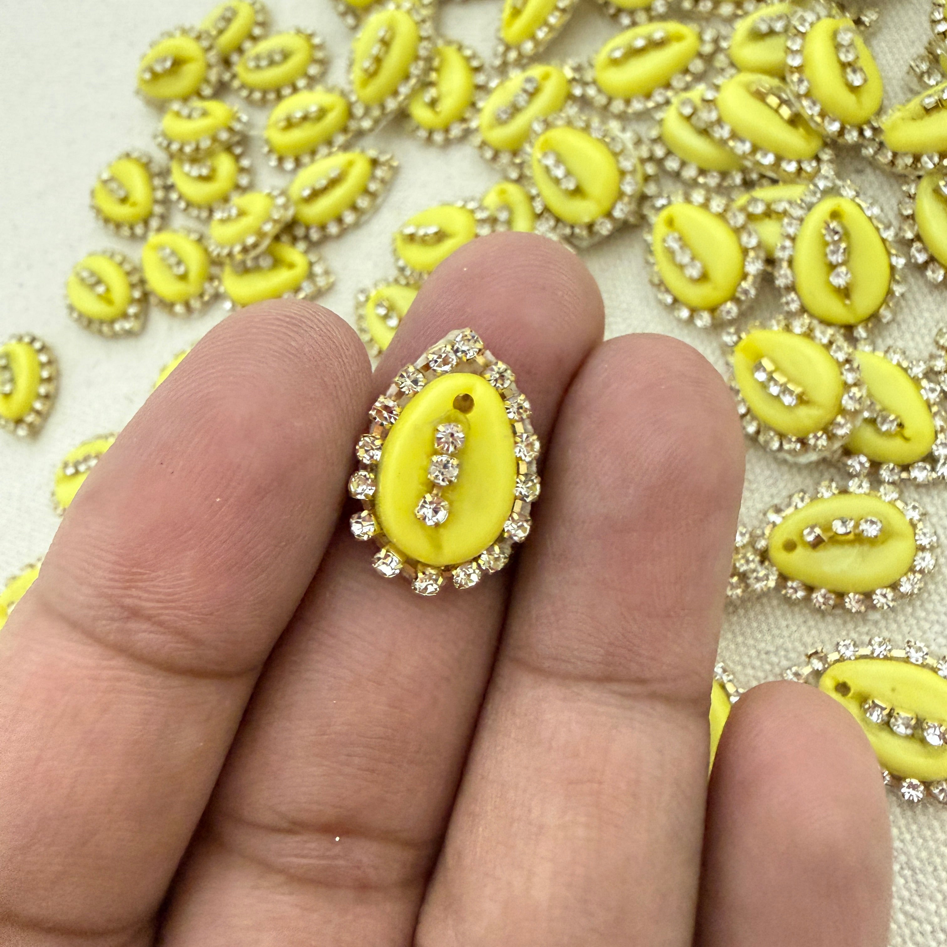 Yellow decorative element with rhinestones held between fingers against a background of similar elements.