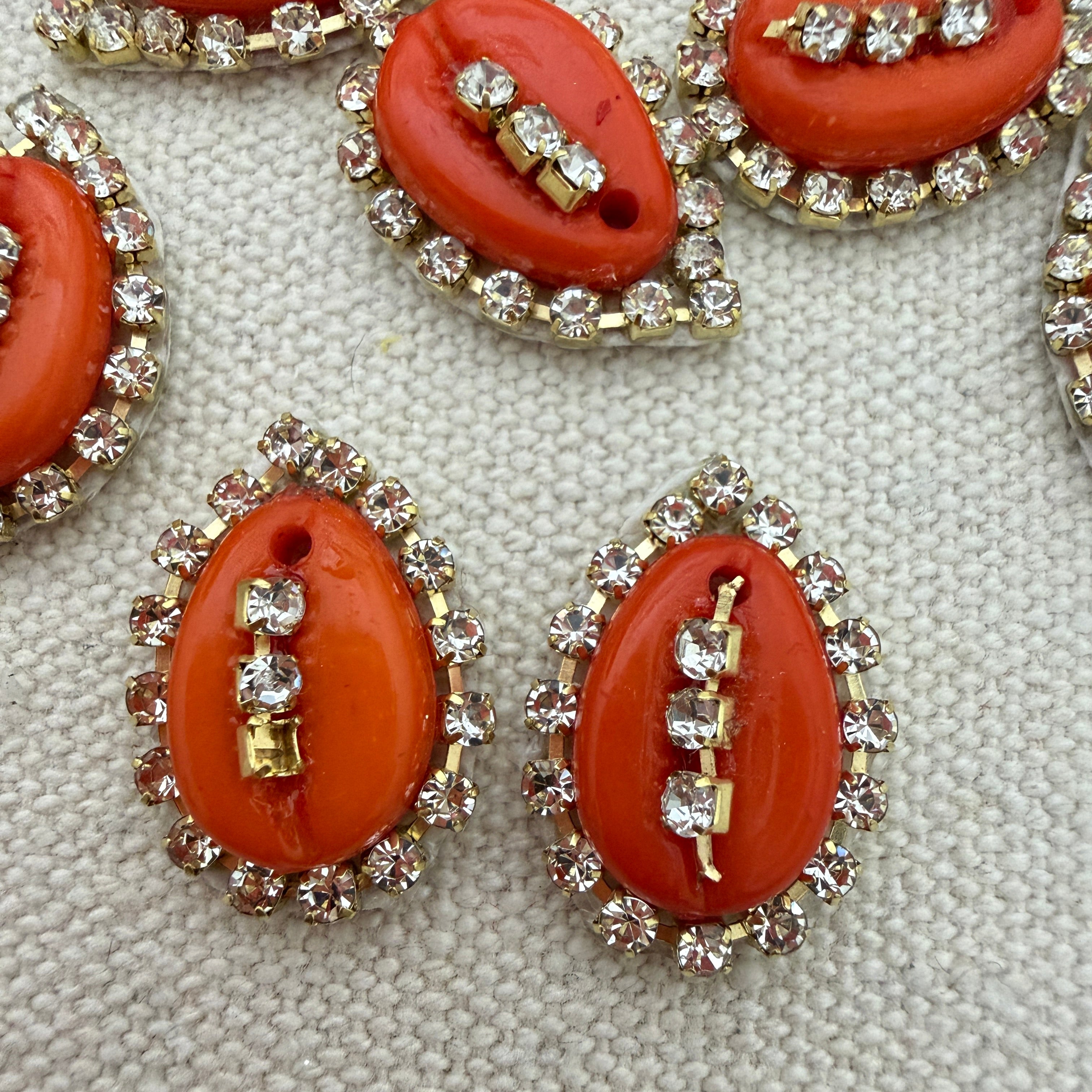 Red oval stones with gold and rhinestone accents on a textured surface