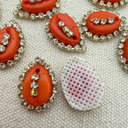 Decorative buttons with coral-colored stones and rhinestones on a textured surface.