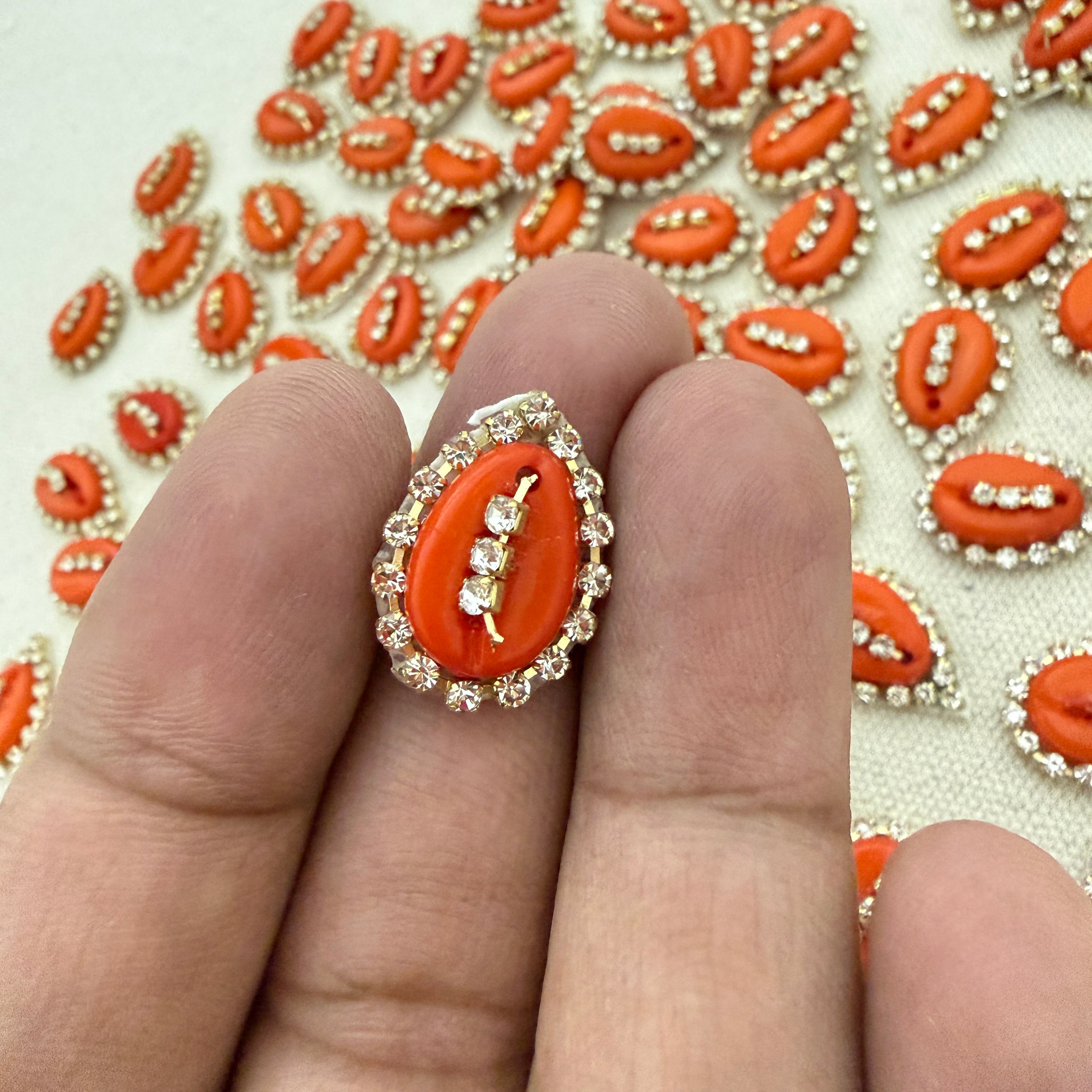 Close-up of a ring with an orange stone and gold accents on a finger, with a background of similar stones.